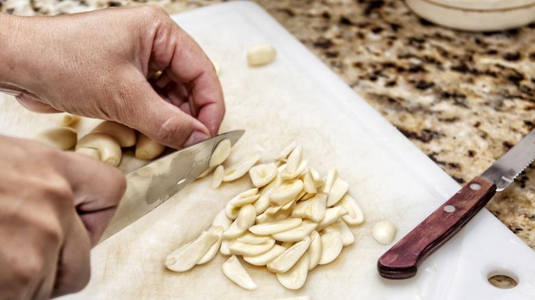 hands chopping garlic on a heavily used plastic cutting board