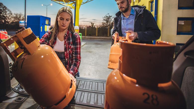 a man and a woman unloading propane tanks under a gas station garage