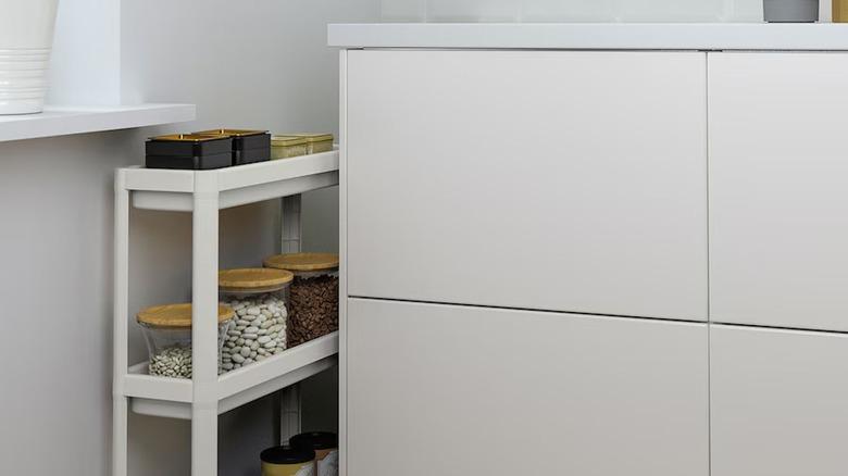 white IKEA VESKEN cart containing containers of pantry staples part way rolled into a small space between a wall and a white kitchen cabinet