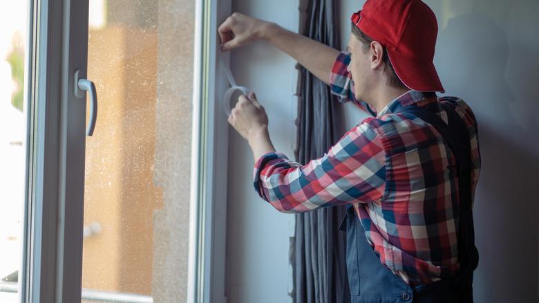 Man in flannel shirt applying Alien Seal tape to windows