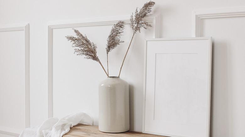 white wall with single layer of wall trim molding behind a small table with potted plant and empty picture frame