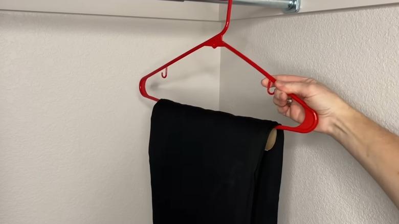 person hanging up a red hanger with cardboard toilet paper tubes wrapped over the bottom, over which a pair of black pants are hanging