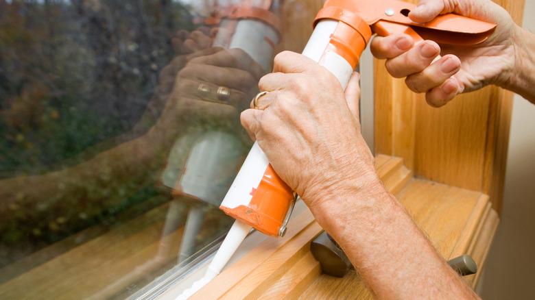 person's hands and forearms applying caulking to a window frame