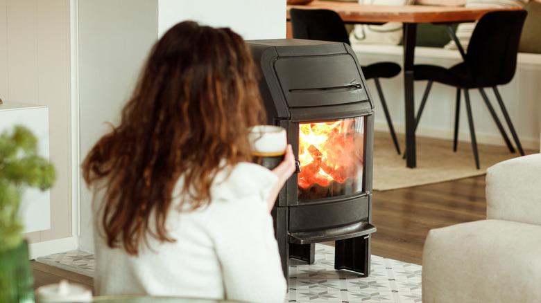 woman sitting near a home fireplace and holding a mug in both hands