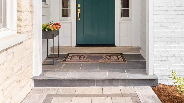 The netryway of a white brick house with a dark green door.