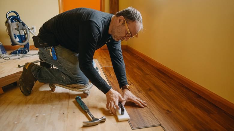 A man is on his knees, installing hardwood flooring.