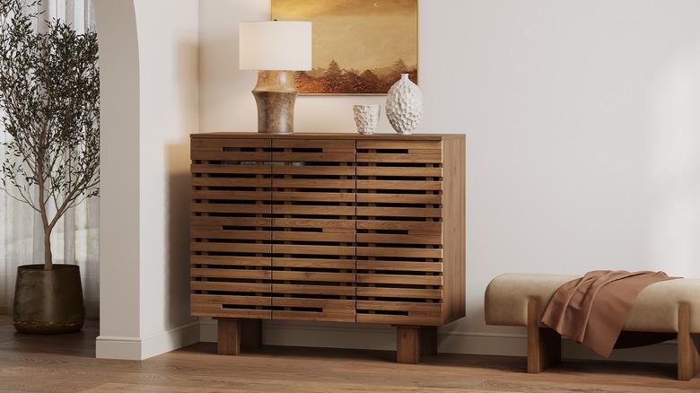 Entryway with medium wood floors, white walls, a taupe bench, and a modern medium wood shoe storage cabinet with horizontal slatted doors