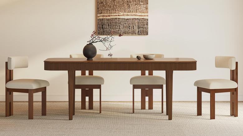 Dining room with off-white walls, cream carpet, a rich stained wood reeded dining table, four mid-century wood chairs with white upholstery, and a woven art piece