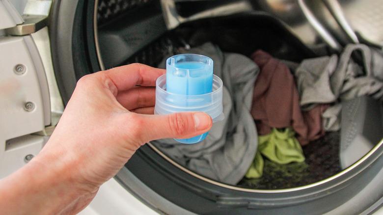 Hand holding liquid fabric softener in front of dryer