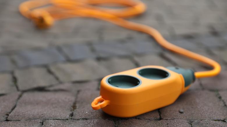 A close-up photo of an orange outdoor extension cord sitting on pavement.