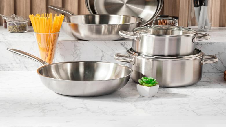 stainless steel cookware on a marble countertop against wooden wall