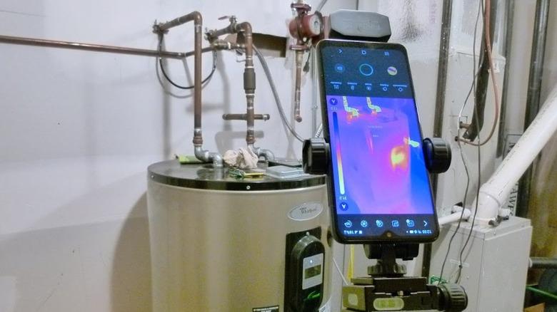 An HSFTOOLS Finder S2 attached to a smart phone faces right faces a hot water heater tank to detect thermal imaging within