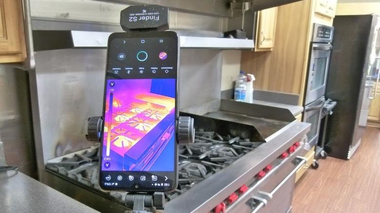 an HSFTOOLS Finder S2 attached to a smartphone is used to detect thermal imaging in a commercial kitchen near a stovetop