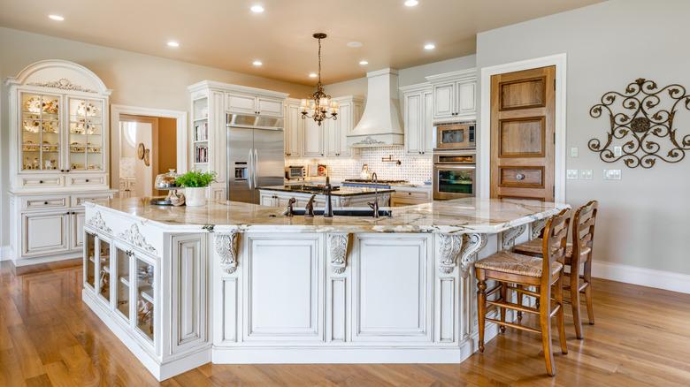 An all-white French Country kitchen with wood accents and ornate scrollwork on the cabinets