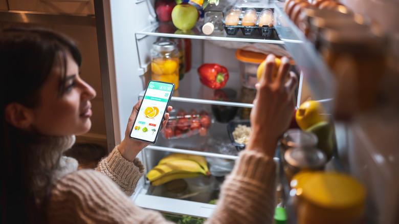 Woman opens smart fridge to check groceries while using phone