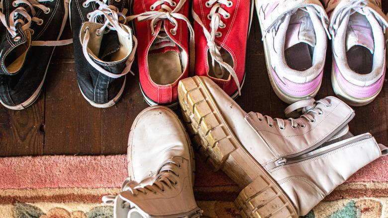 three pairs of sneakers and one pair of boots cluttering the wood floor with pink floral rug