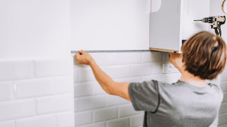 person measuring the top of a white subway tile kitchen backsplash from wall to upper cabinet