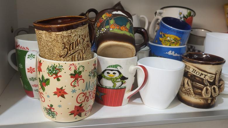 A cluttered kitchen cabinet filled with poorly stacked Christmas mugs