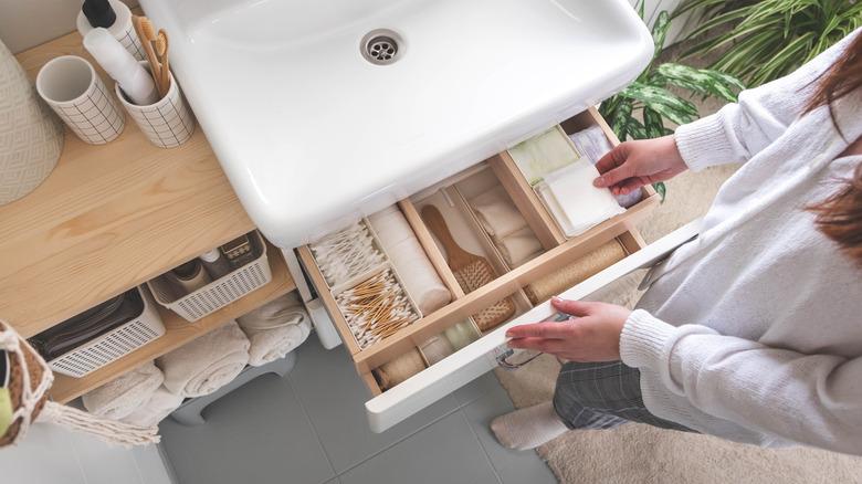 a person pulling out a perfectly organized drawer underneath their bathroom sink, with bathroom storage on the side