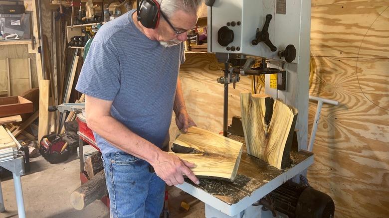 man wearing ear protection holding piece of wood at bandsaw