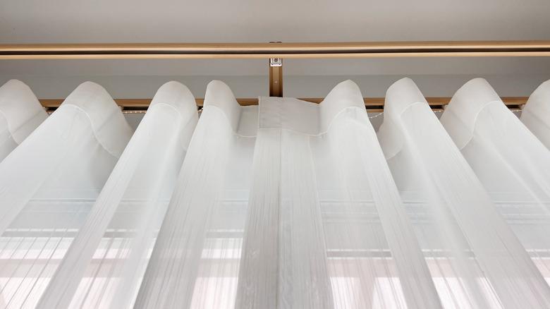 An upward angle of white sheer drapes on a curtain rod.