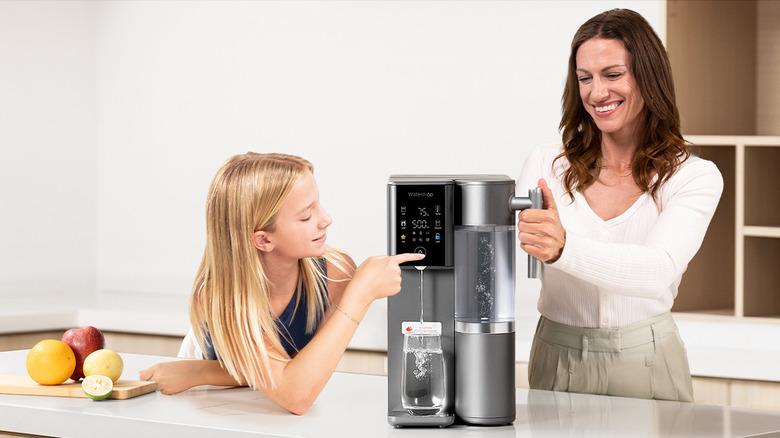 Mother and daughter operating a Waterdrop Filter A2 reverse osmosis water dispenser  on the kitchen island by dispensing a cup of water into a glass