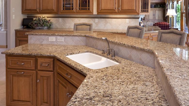 outdate kitchen with honey oak cabinets, an angled two-tier island, and brown and beige speckled granite countertops