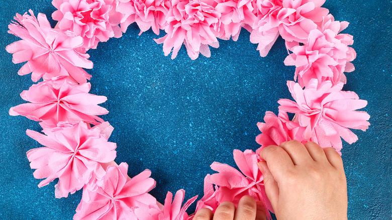 Hands adding pink paper flowers to a heart-shaped wreath