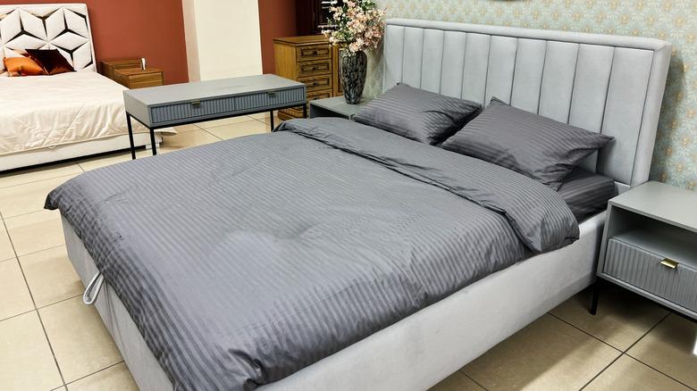 A bed on a showroom floor dressed in matching gray-ticked sheet, pillows, and blanket.