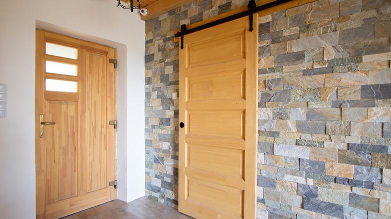 The corner of a room with a light wood exterior door, and a matching interior sliding barn door. One wall is painted white, and the other is covered in colorful slate.