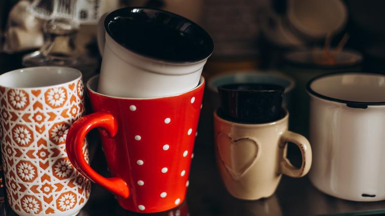 collection of variety of coffee and tea mugs stacked haphazardly