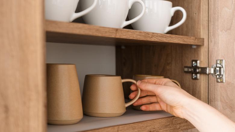 Hand reaching for mugs in cupboard