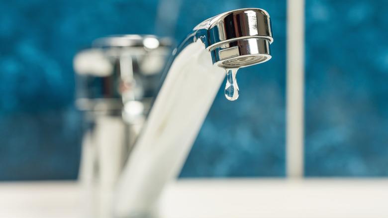 An indoor faucet for a bathroom or kitchen slowly drips one big droplet of water.