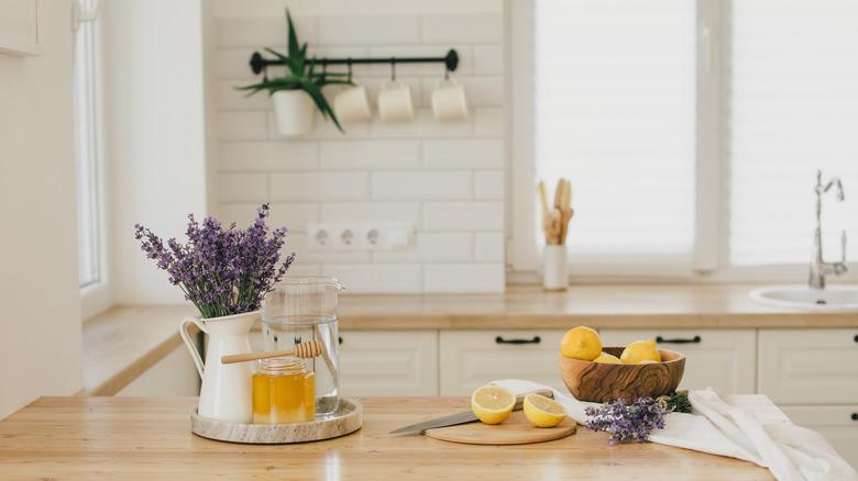 A vase of fresh lavender, bowl of lemons, and jar of honey sit on the counter in an all-white kitchen.