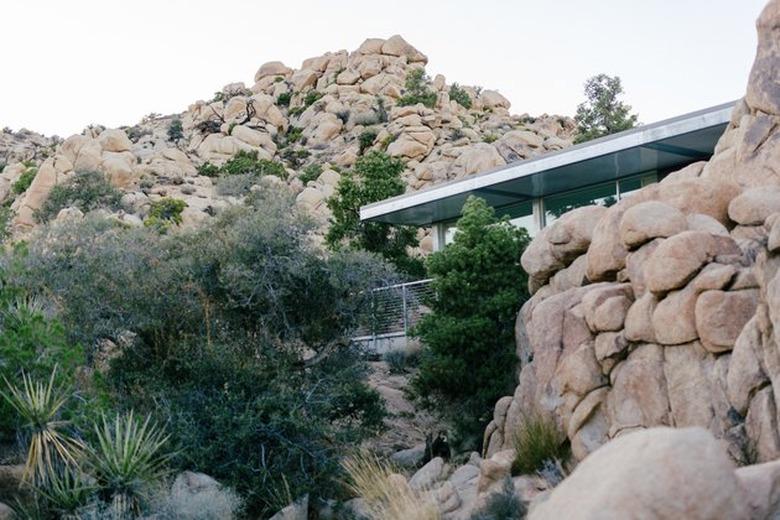 modern midcentury-style prefab house set within large desert boulders