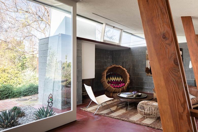 Mid-century living room with large glass windows, wood beams, and maroon floors