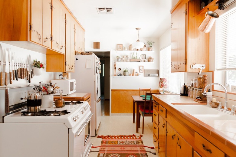 Wood cabinets in kitchen with traditional rug, wood dining furniture by white shelves with plants and pottery.