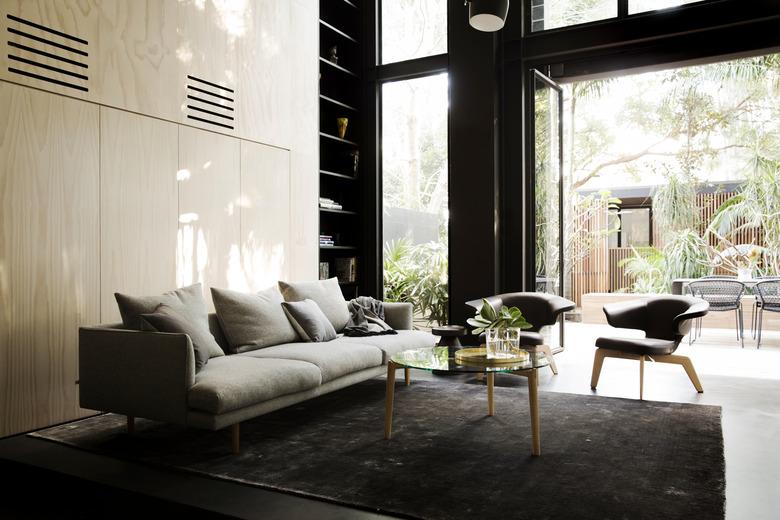 Living room with gray couch, gray chairs, plywood wall, and big windows.