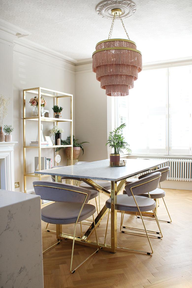 Pink and white art deco dining room with pink fringe chandelier and blue velvet chairs