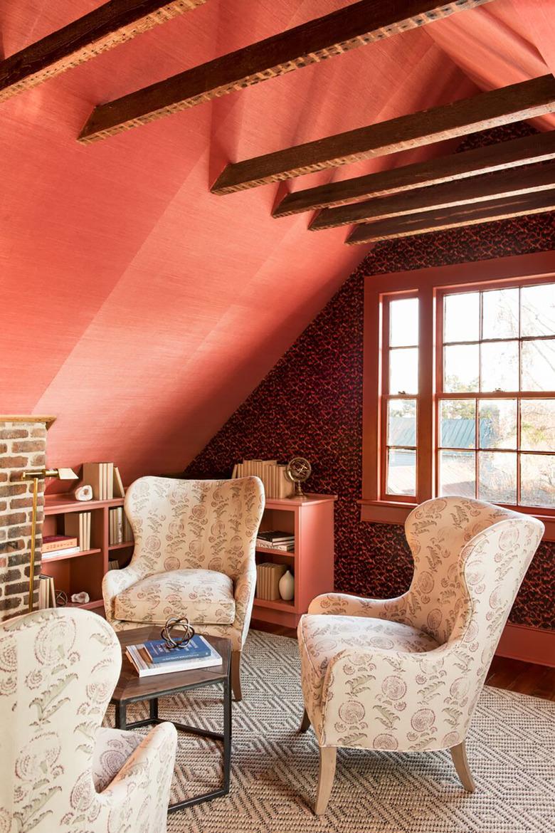 attic apartment with red-orange wallpaper, patterned wallpaper, wood beams, high back chairs, patterned rug.