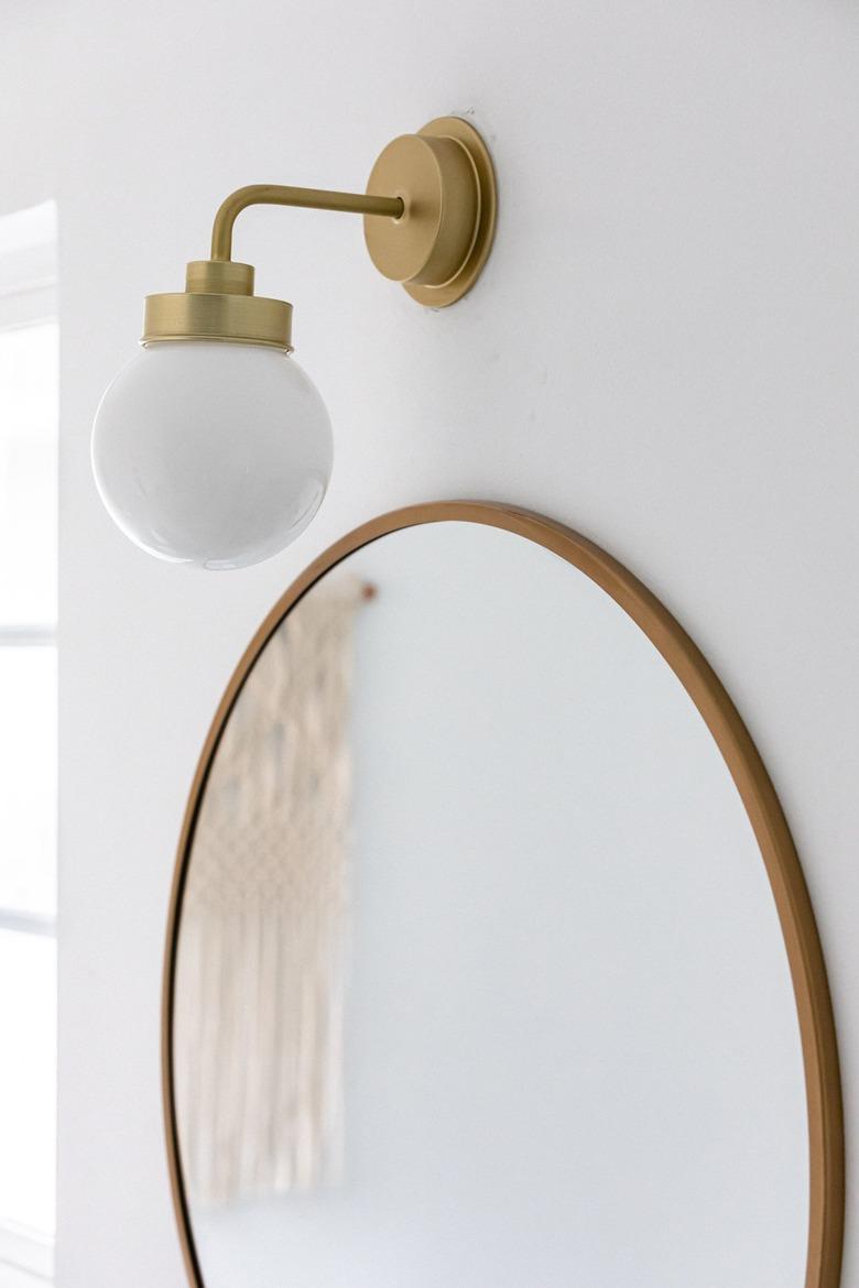 A large round bathroom mirror with a globe light fixture