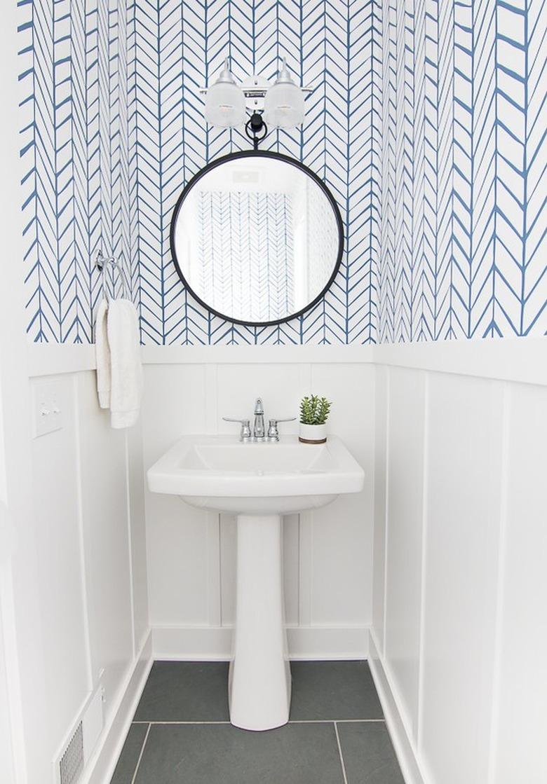 bathroom space with blue and white wallpaper and round mirror