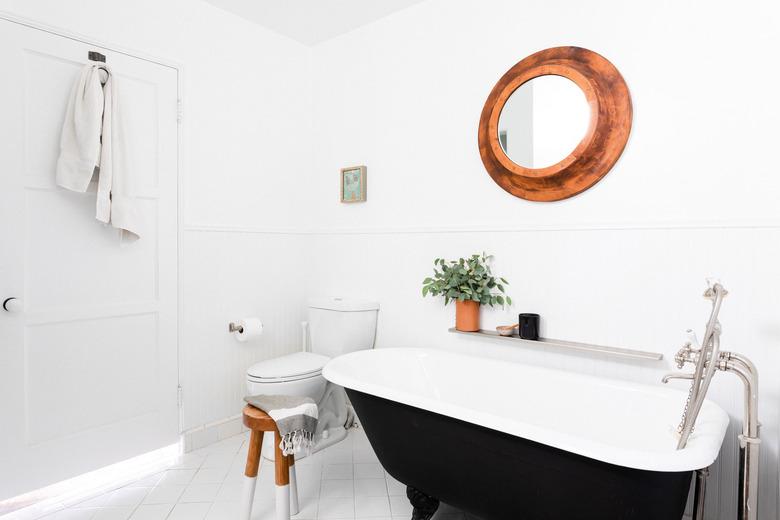 bathroom with black clawfoot tub, toilet and circular mirror