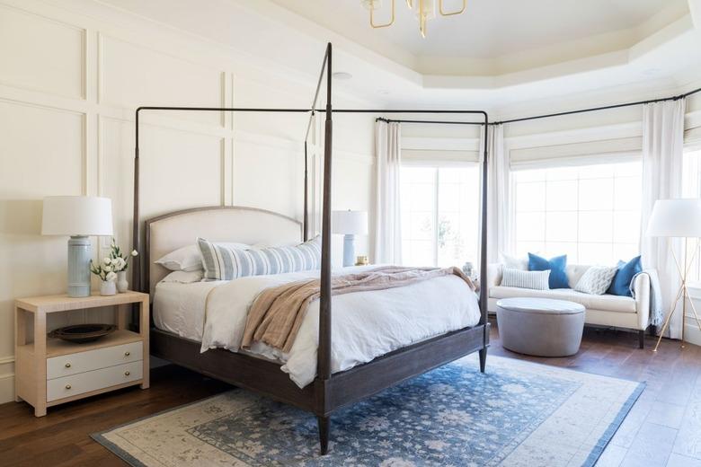 white bedroom with wall paneling and white bay window curtains and shades