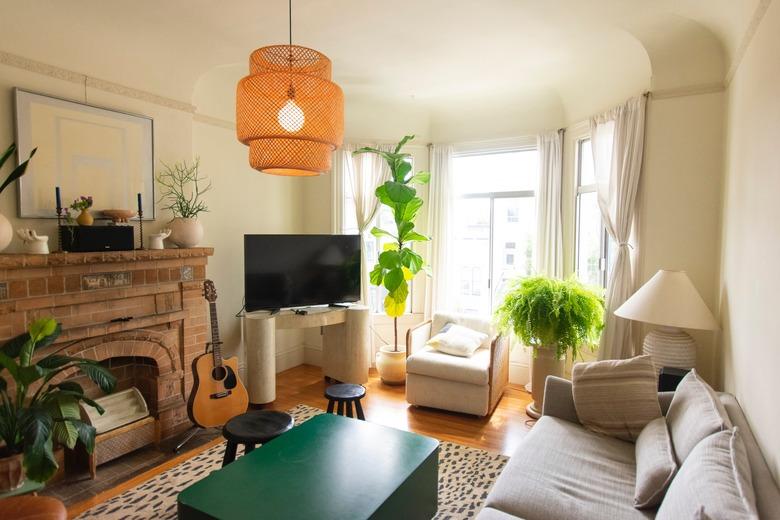 Living room with exposed brick fire place, plants, and bay window curtains