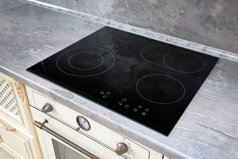 Modern kitchen interior with black induction or electric hob stove cooker with ceramic top surface with marble countertop and wall decorated with stone.