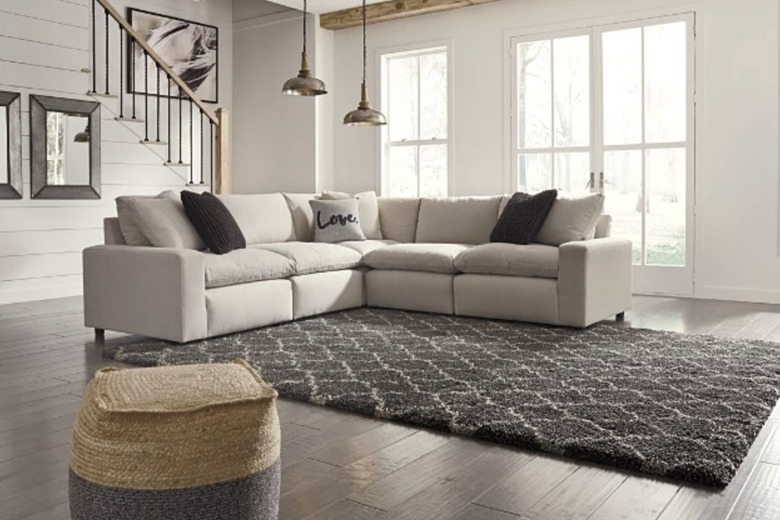 Beige couch in room with wood floors and white walls. There is a brown rug and a seagrass ottoman on the floor