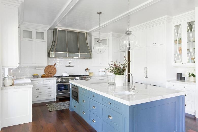 blue kitchen island in all-white space with dark wood flooring