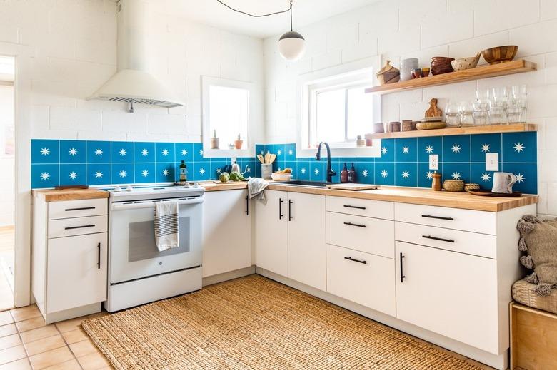 a kitchen with white cabinets, white walls, and a backsplash made of large azure tiles each with a star in the center