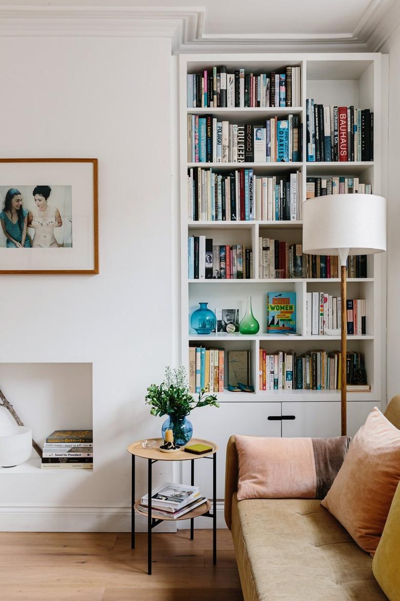 book storage in modern living room with bookshelves, leather couch, lamp, small side table, and small white fireplace underneath hung framed picture